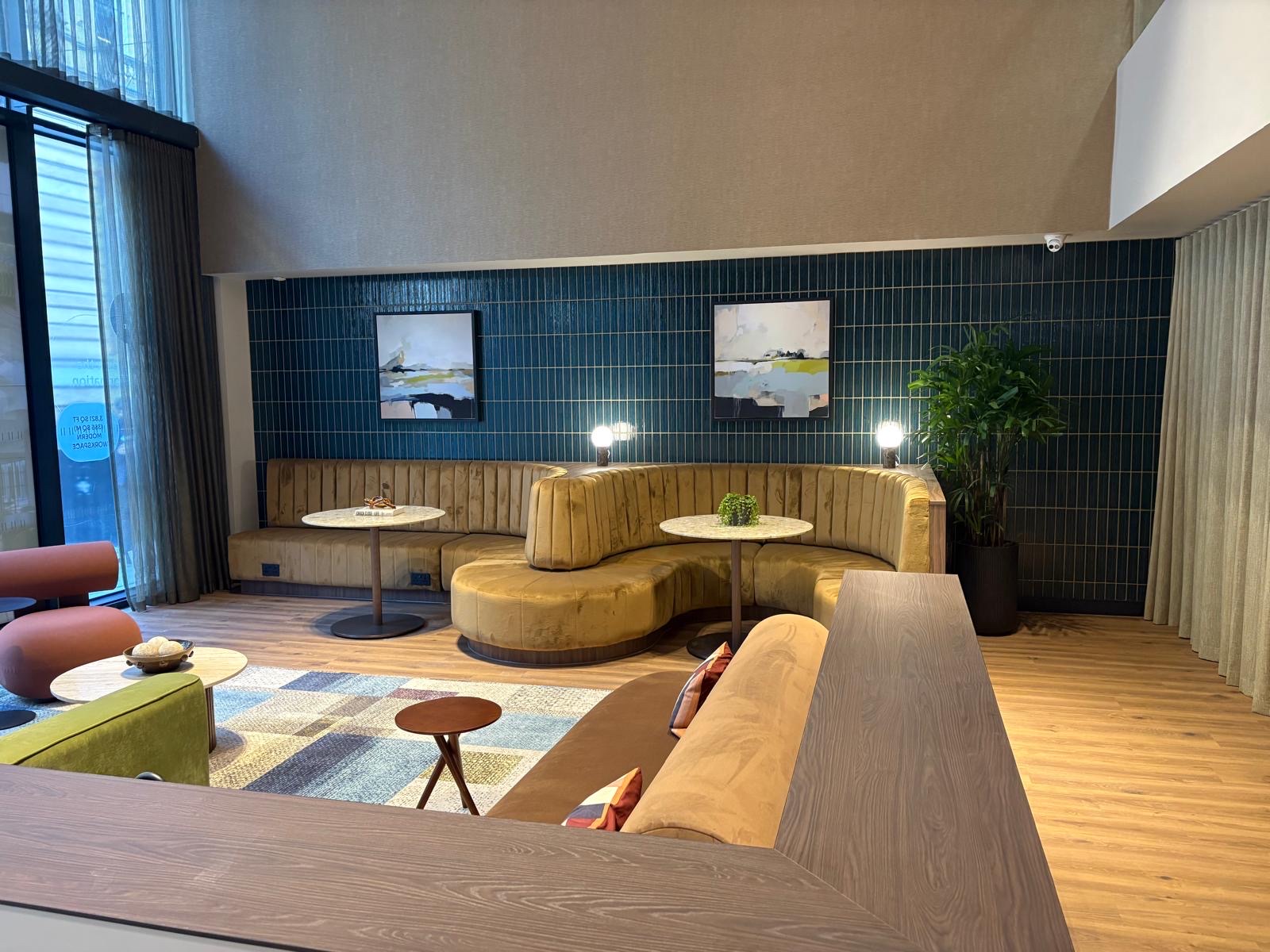 Commercial reception lounge with a deep teal vertical stacked tile feature wall behind curved velvet banquette seating