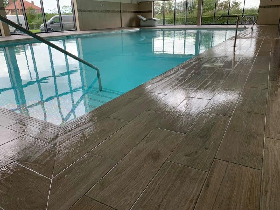 Indoor swimming pool surround tiled in wood-effect porcelain planks with a mosaic pool interior