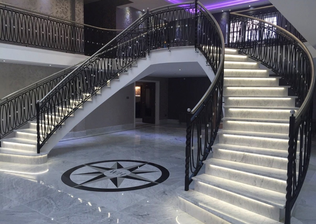 Grand twin curved staircase with LED-lit marble treads above a polished marble floor with an inlaid compass rose medallion