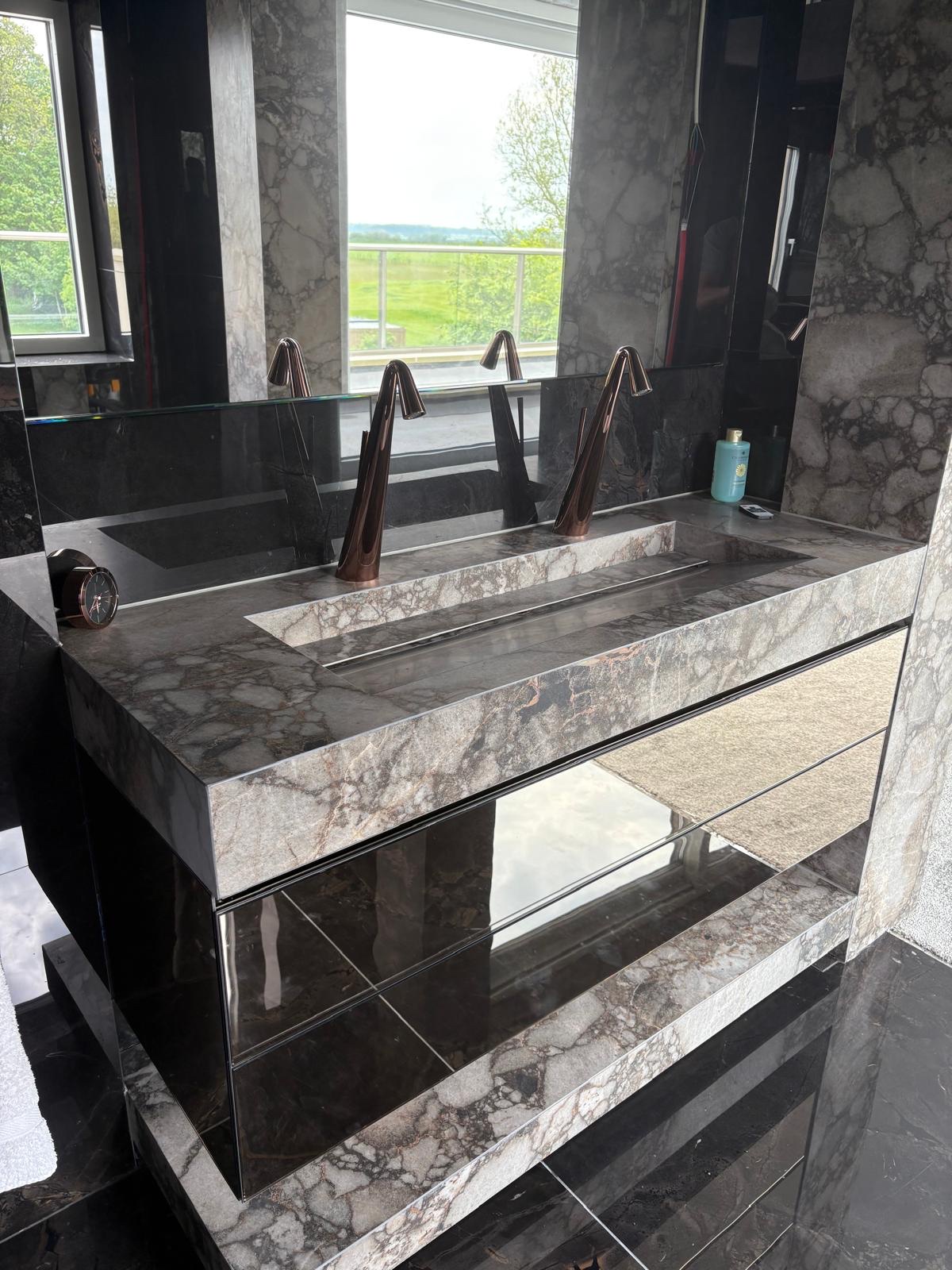 Double trough basin vanity fabricated from marble-effect porcelain with mirrored drawers and rose gold taps