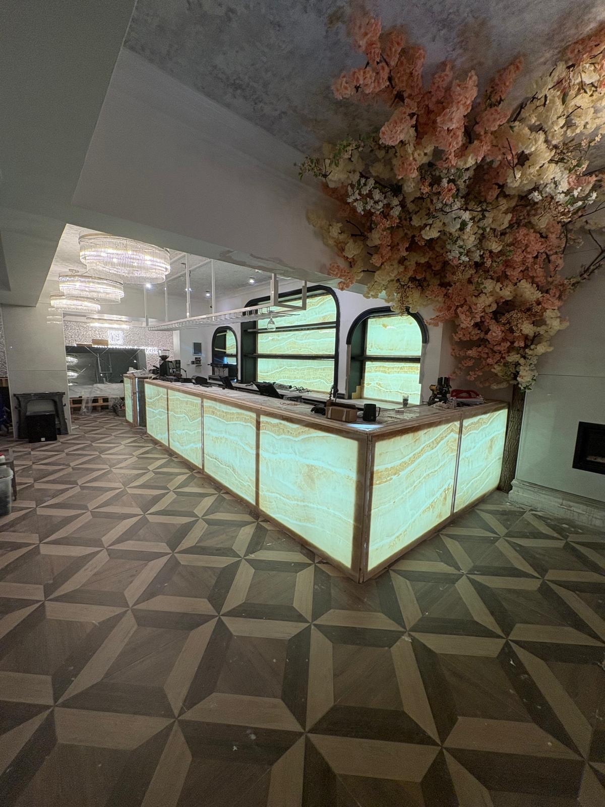 Restaurant bar clad in backlit onyx-effect panels above a geometric parquet-pattern porcelain floor