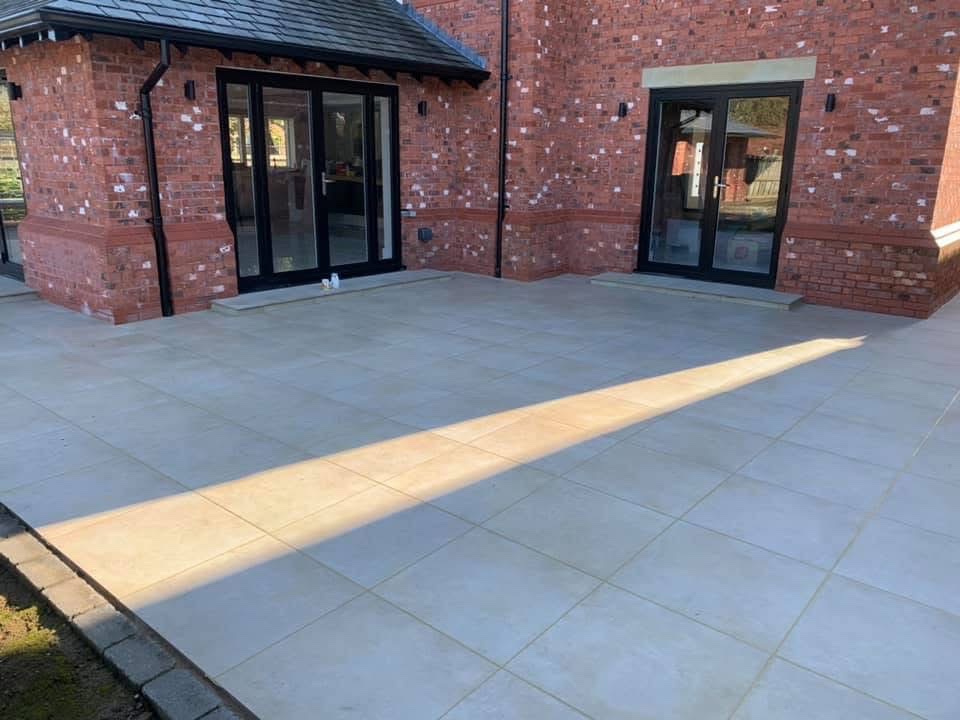 Outdoor patio laid in large-format grey porcelain paving behind a red brick house with French doors