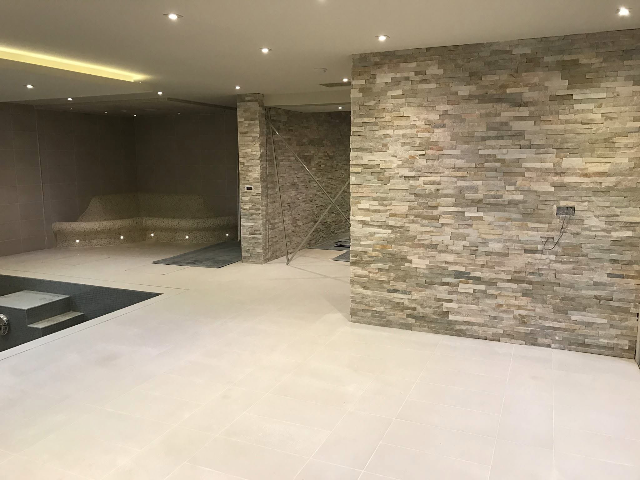 Basement spa with large-format pale porcelain floor and a split-face natural stone feature wall
