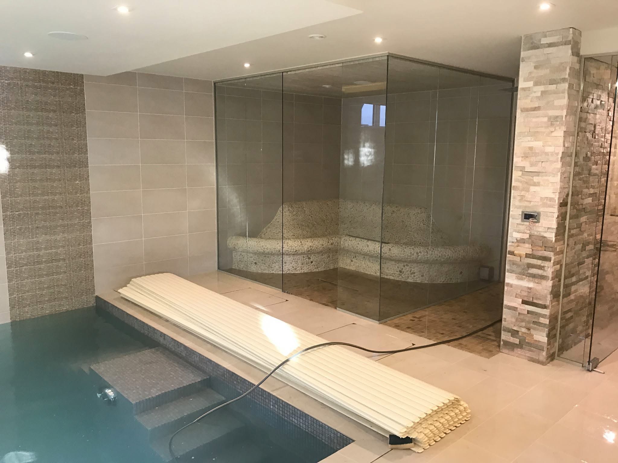 Glass-fronted steam room with a curved pebble mosaic bench next to a mosaic-lined plunge pool and split-face stone pillar