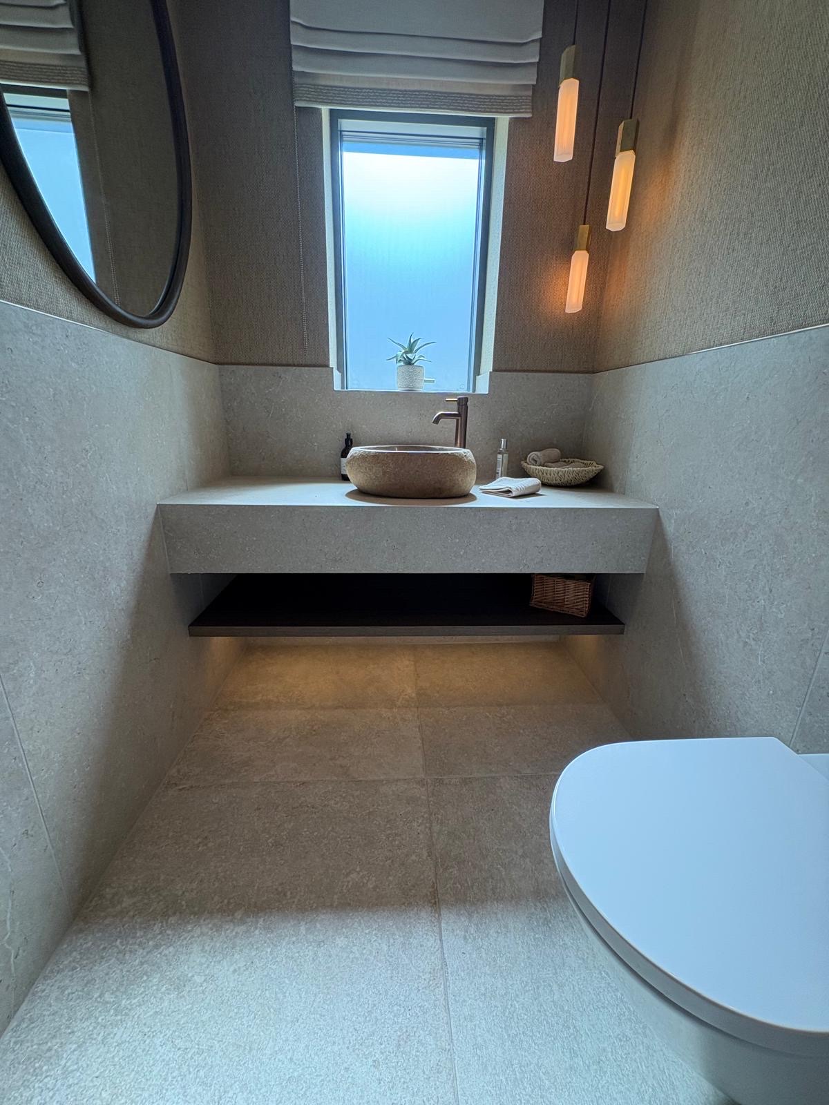 Cloakroom with stone-effect porcelain walls and floor and a floating tiled vanity holding a stone basin